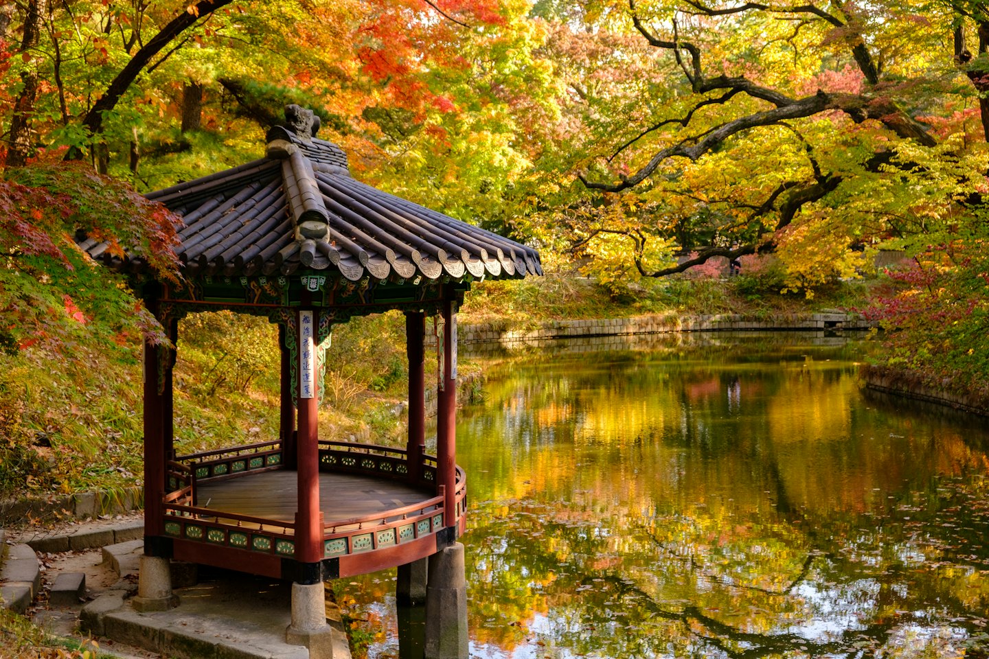 Hölzerner Pavillon neben einem Teich mit Herbstlaub.