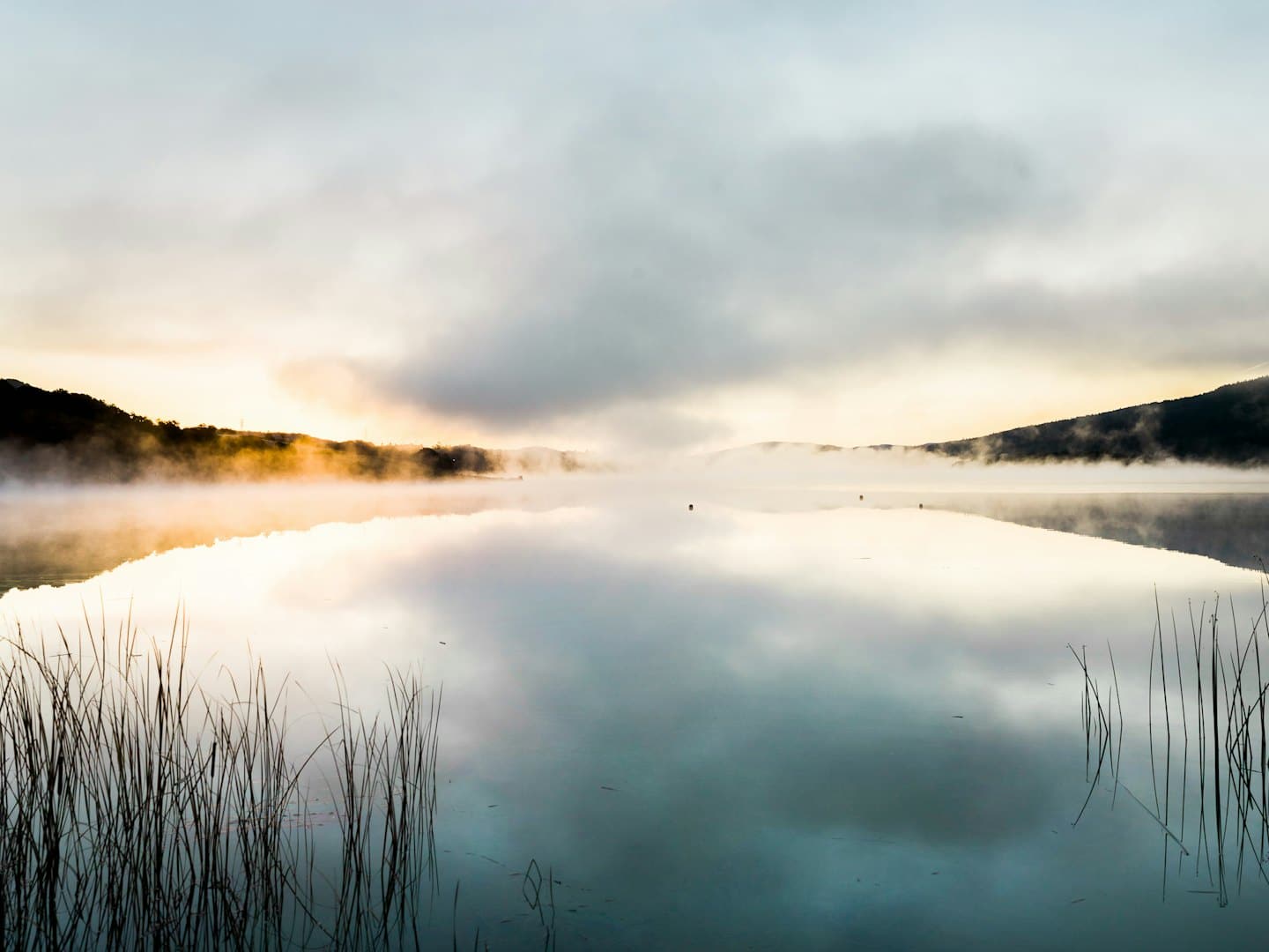 Nebel steigt über einen ruhigen See mit Hügeln in der Ferne.